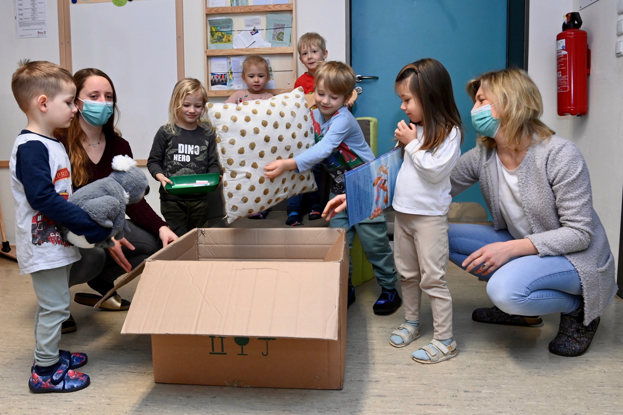 Mehrere Kinder sitzen gemeinsam auf dem Boden eines Gruppenraums. Spielmaterial liegt in der Mitte.