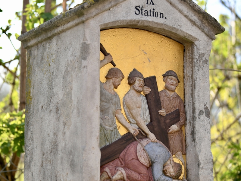 Steinkapelle mit Kreuz auf dem Dach, die die siebte Station des Kreuzwegs darstellt. Die Nische zeigt Jesus, der unter dem Kreuz zusammenbricht, umgeben von Soldaten und weinenden Frauen. Die Inschrift lautet "Jesu f&auml;llt das 2te mal unter dem Kreuze.