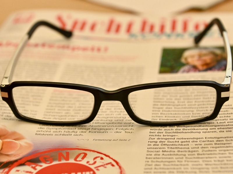 Detailaufnahme eines Schreibtisches mit Brille und Notizmaterial.